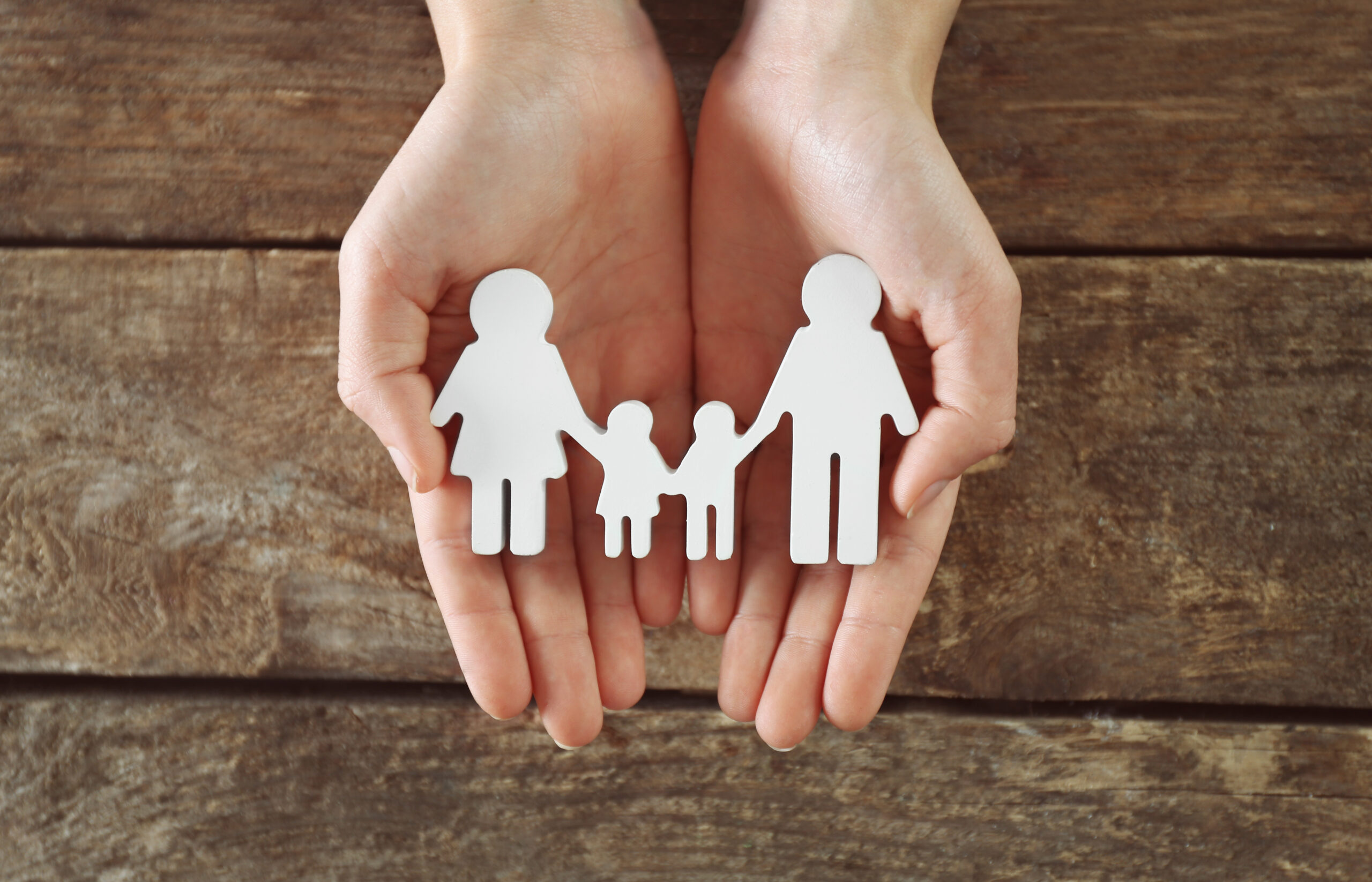 Female hands holding family figure on wooden  background